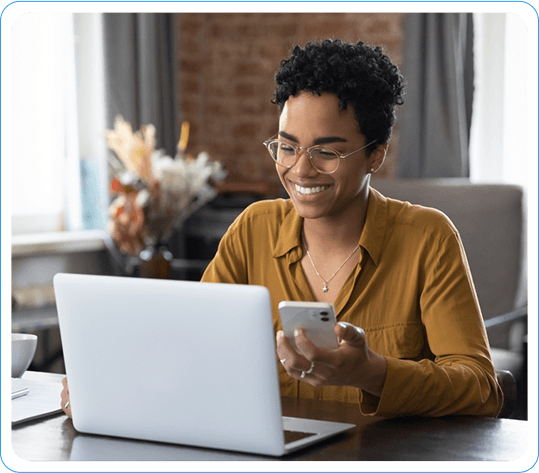 Smiling Woman Managing Customer Account on Laptop and Smartphone While Working from Home in a Cozy Room